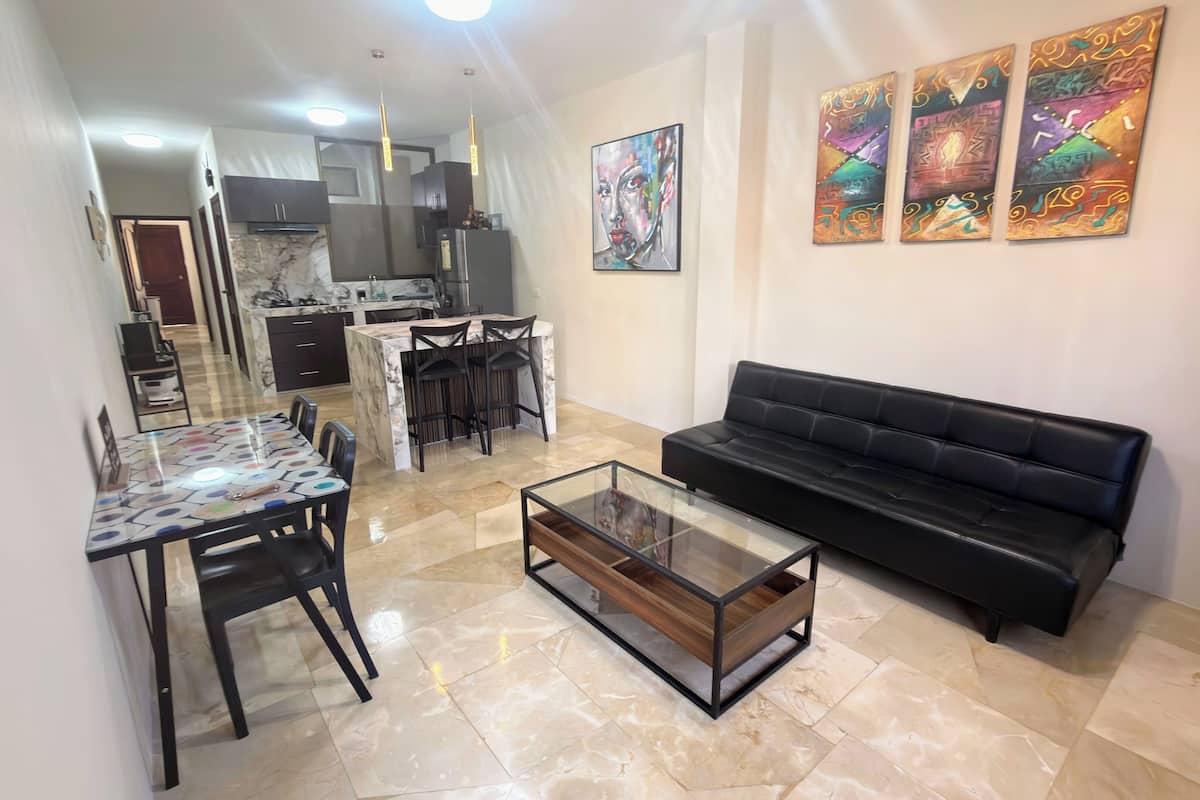 A modern living room with a black sofa, a glass coffee table, and a dining area with a patterned table.