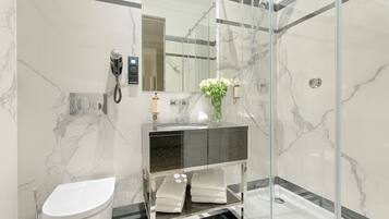 A modern bathroom with a glass-enclosed shower, a marble-tiled wall, a black and white vanity, and a toilet.