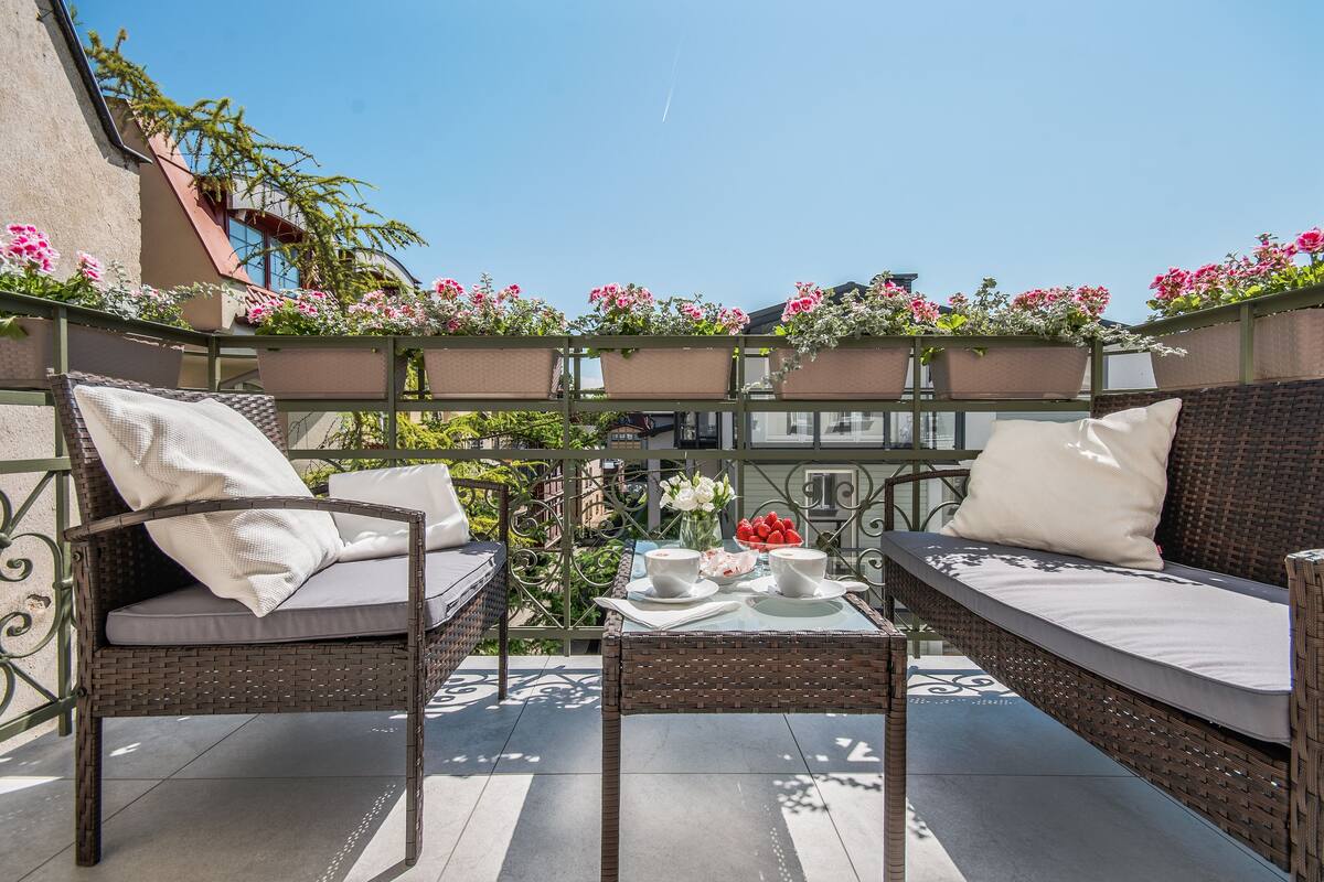 Un balcon agrémenté de meubles en osier, une table avec des tasses et un saladier, et des plantes en pot.