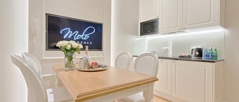 A modern kitchen with white cabinetry, a wooden dining table, and a neon sign on the wall.