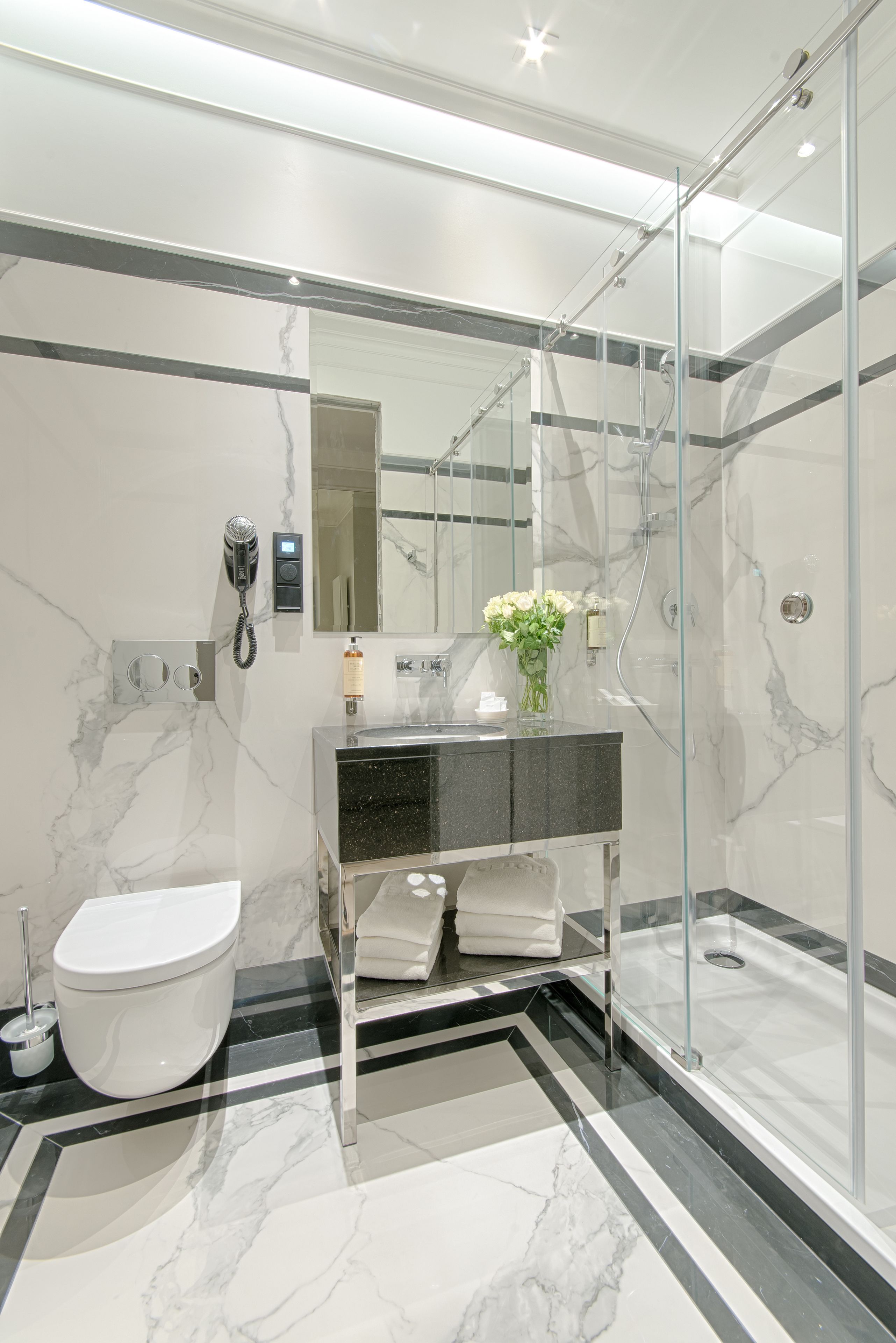 A modern bathroom with a glass-enclosed shower, a marble-tiled floor, a white toilet, and a vanity with a mirror.