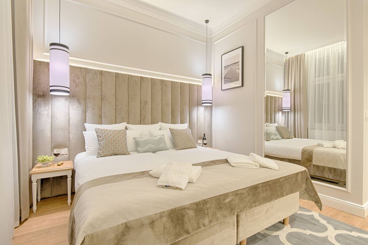 Une chambre d’hôtel moderne avec un grand lit, des tables de chevet, un miroir et une vue sur la ville par la fenêtre.