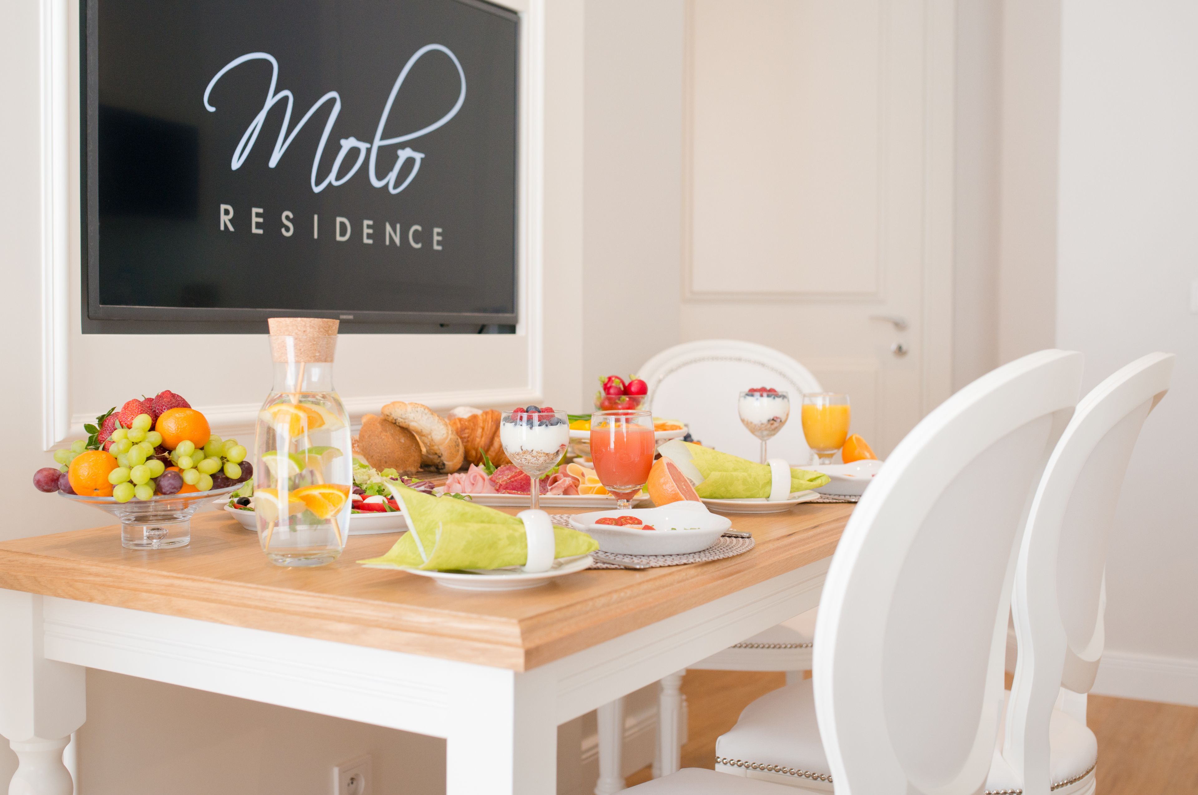 A breakfast table with fruits, pastries, and beverages, a corked bottle, and a sign reading "Molo Residence".