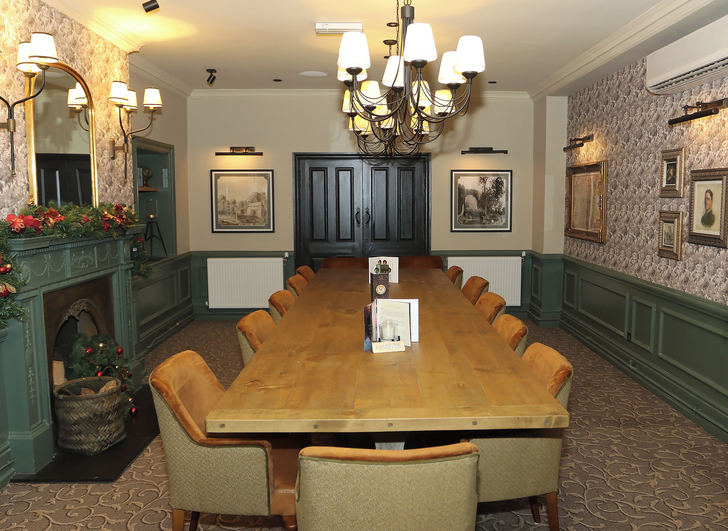 Une salle de conférence avec une longue table, des chaises, un lustre, des tableaux encadrés et une cheminée décorée.