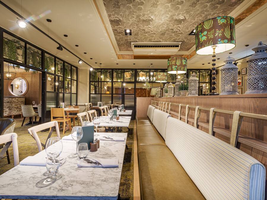 Ein Restaurant mit langen Gemeinschaftstischen, hohen Decken und hängenden Pflanzen.