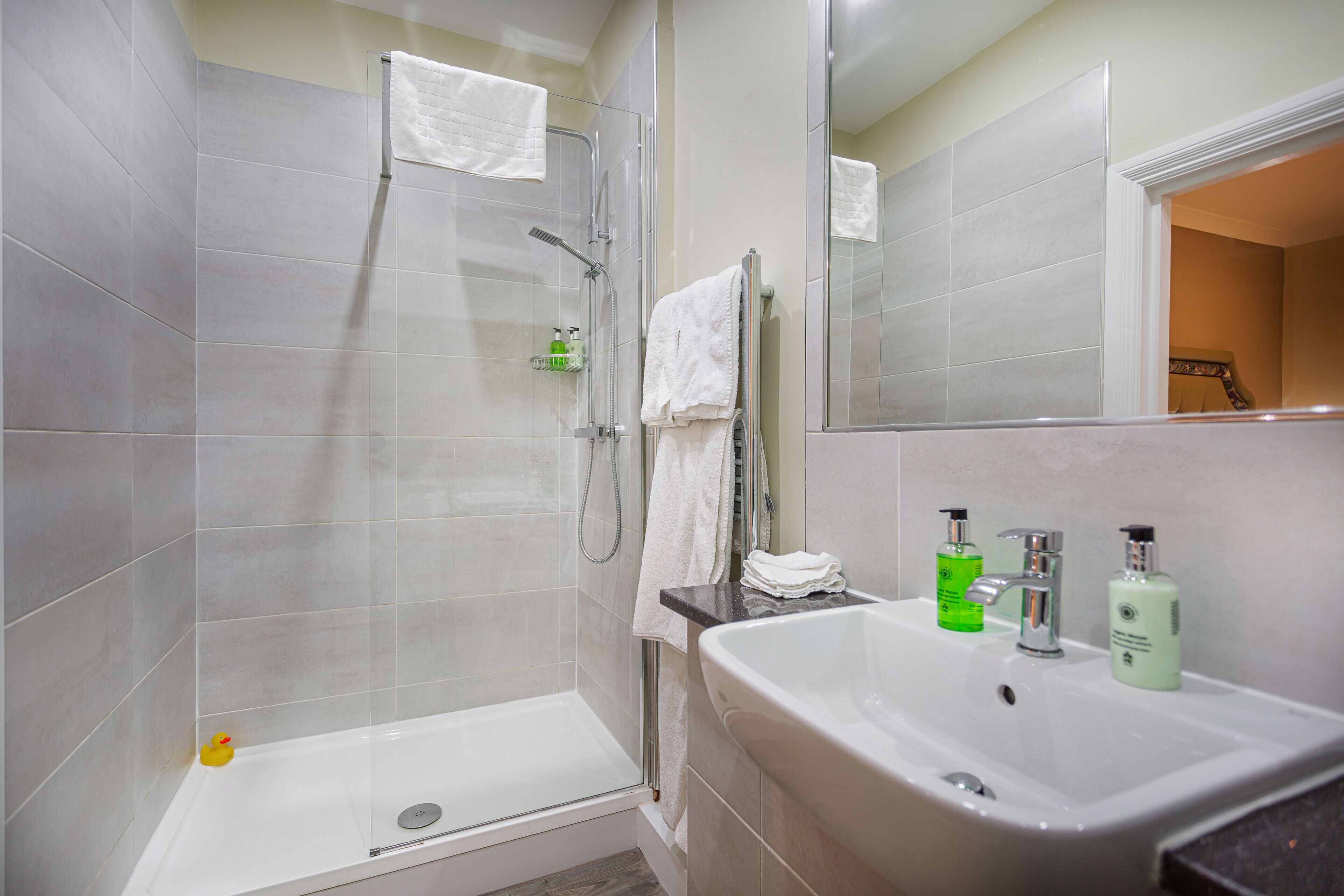 A modern bathroom with a glass-enclosed shower, a white sink with toiletries, and a mirror above the sink.