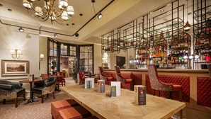 A bar area with a wooden table, red upholstered chairs, and a variety of bottles on shelves. - Wynnstay Hotel, Oswestry, Shropshire (Oswestry)