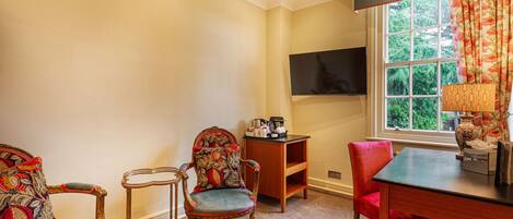 A room with a TV mounted on the wall, a wooden table, two chairs, and a window with curtains.