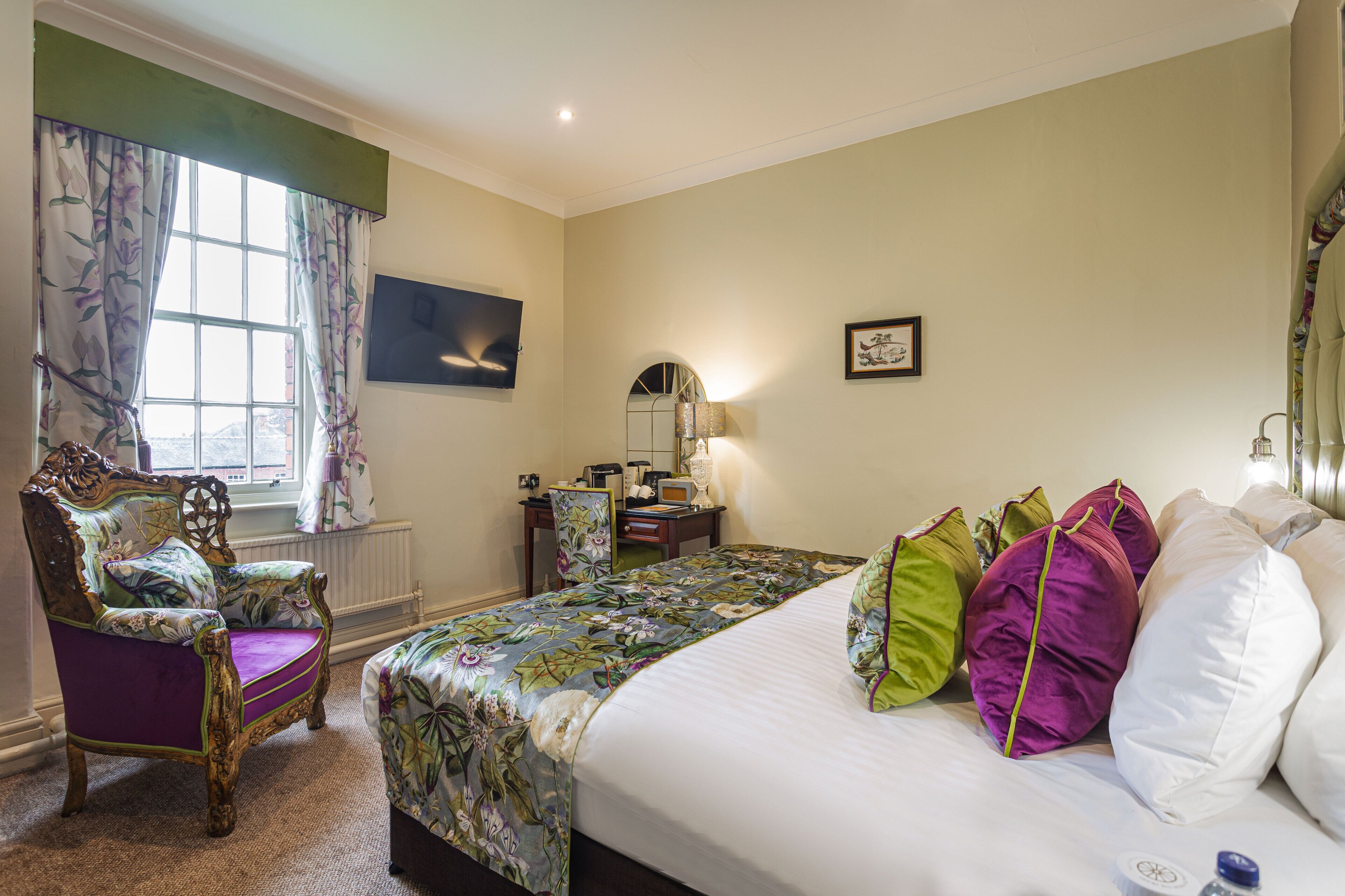A hotel room with a bed, a chair, a desk, a window with curtains, and a wall-mounted TV.