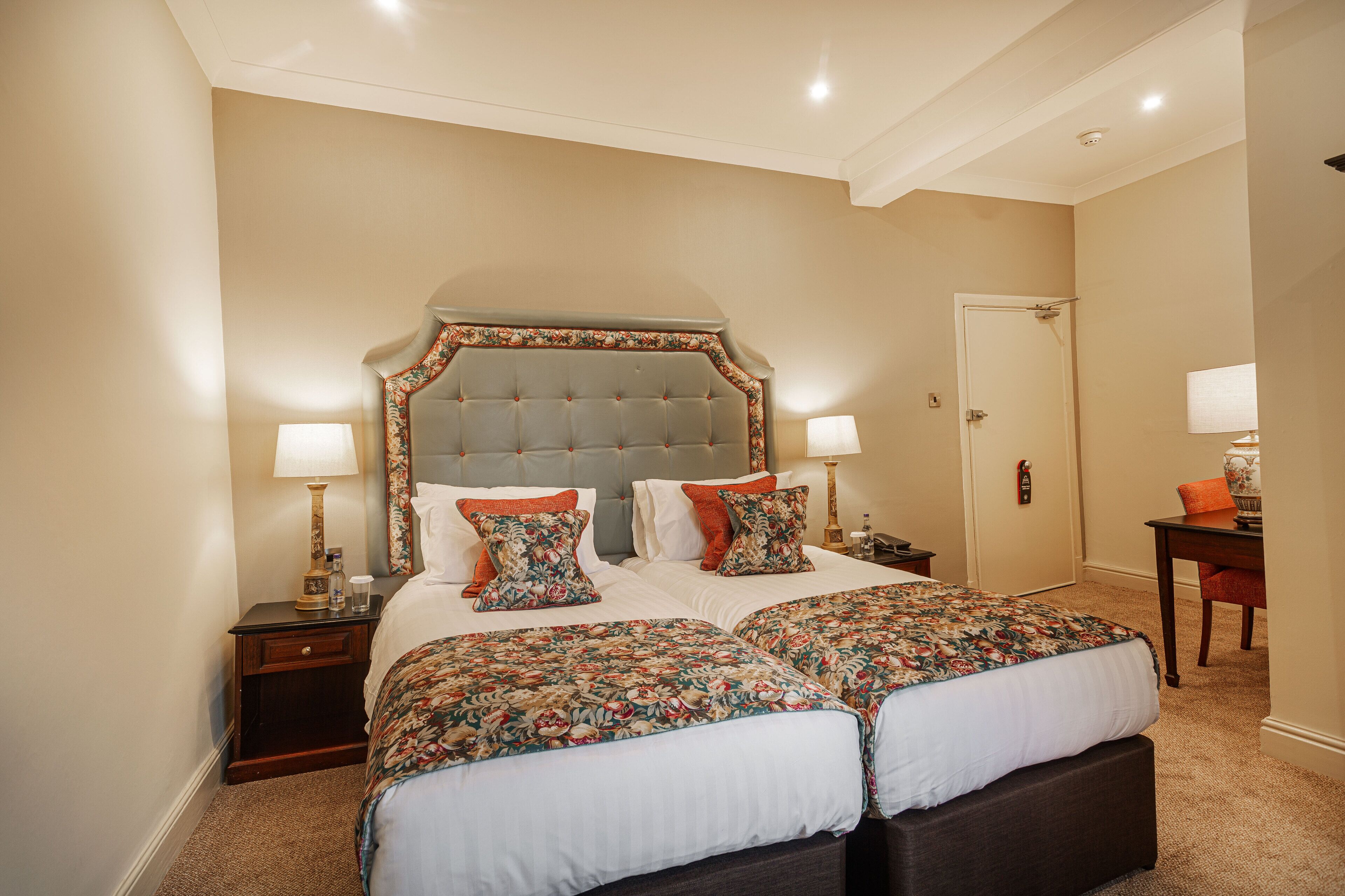 A large bed with a tufted headboard, two bedside tables with lamps, and a door in the background.