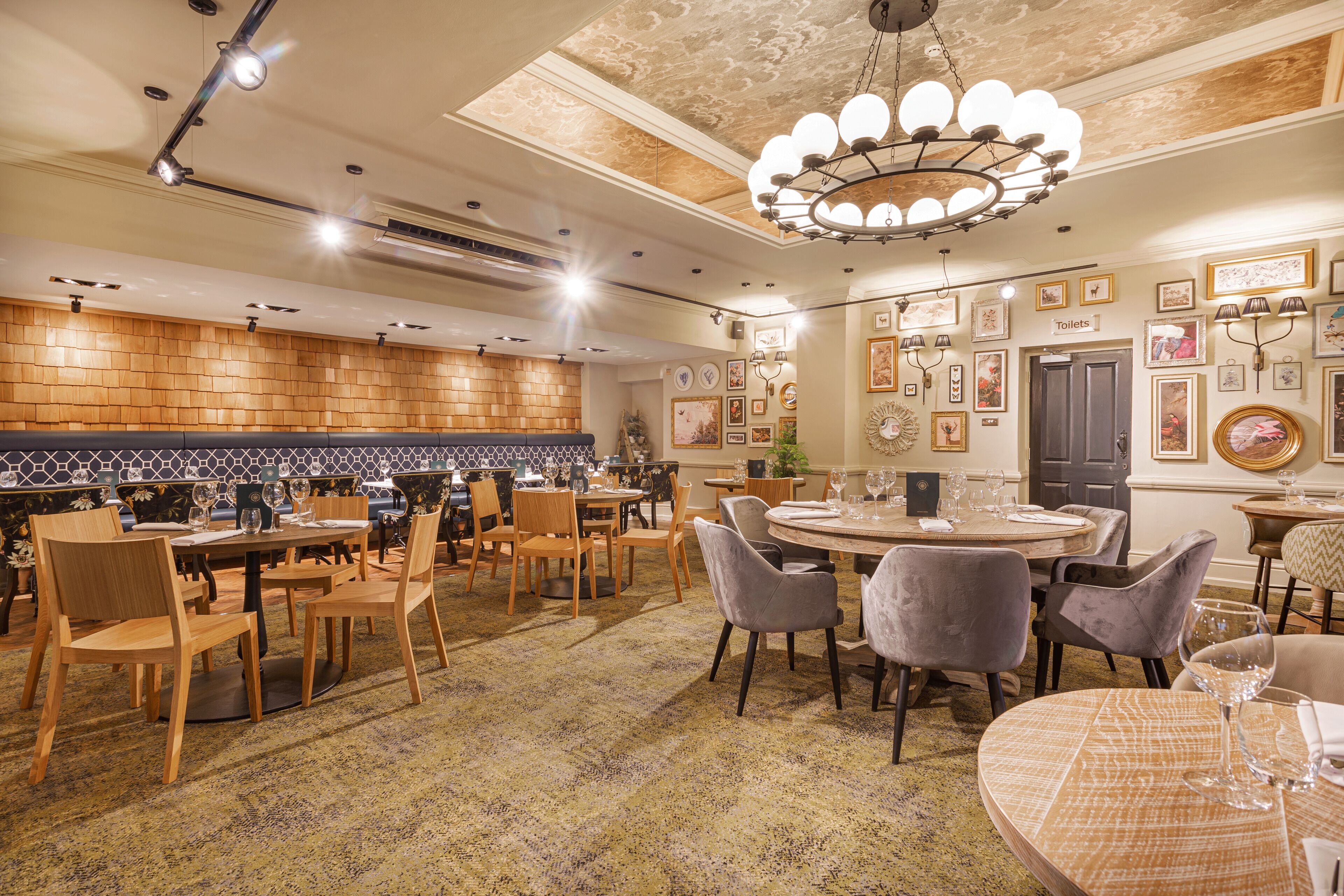 Um restaurante com mesas e cadeiras de madeira, um tapete estampado e um candelabro.