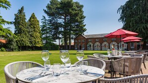 Outdoor dining tables with chairs, a brick building, and a lawn in the background. - Wynnstay Hotel, Oswestry, Shropshire (Oswestry)