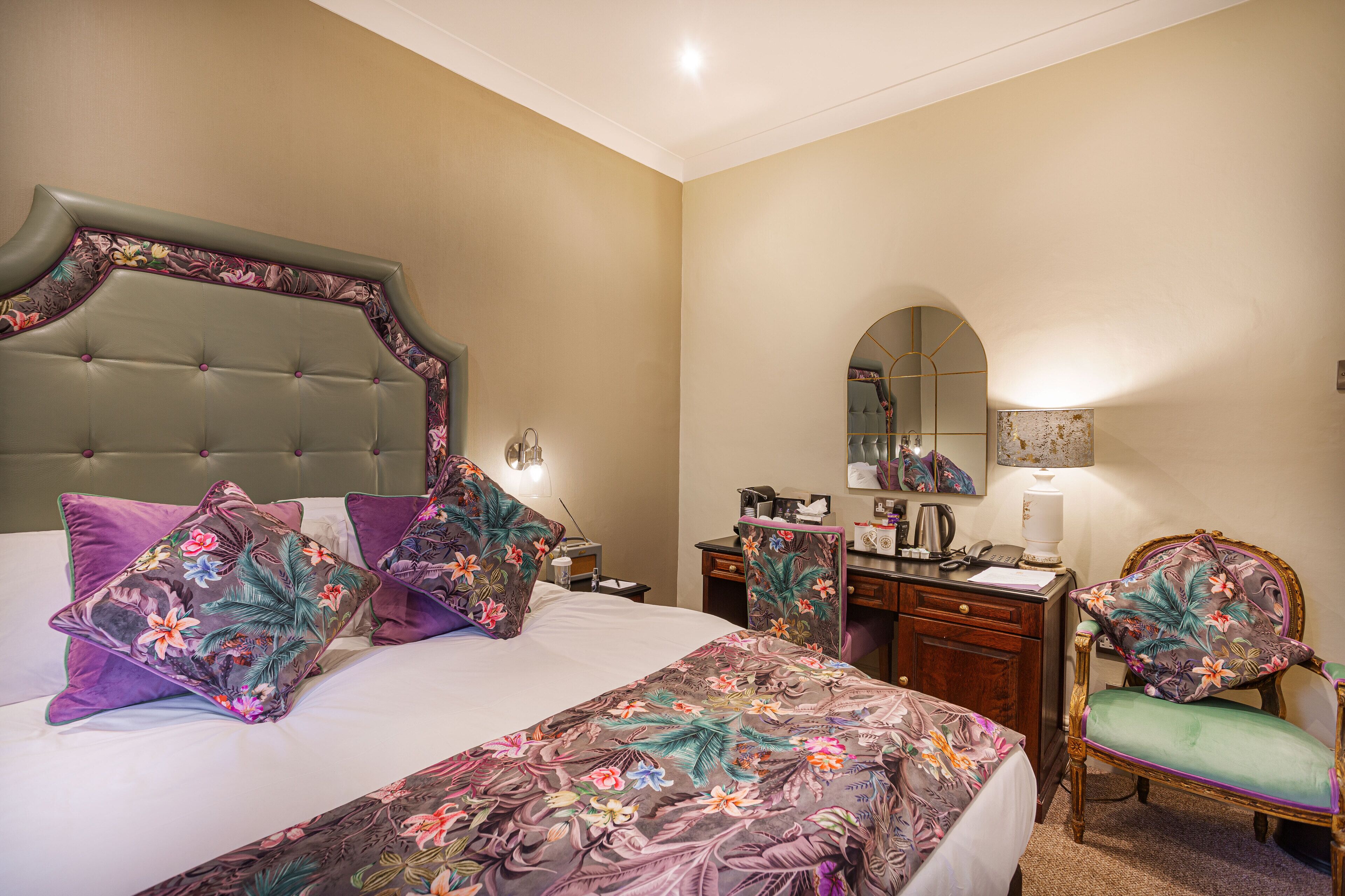 A hotel room with a large bed, a desk, a chair, and a mirror.