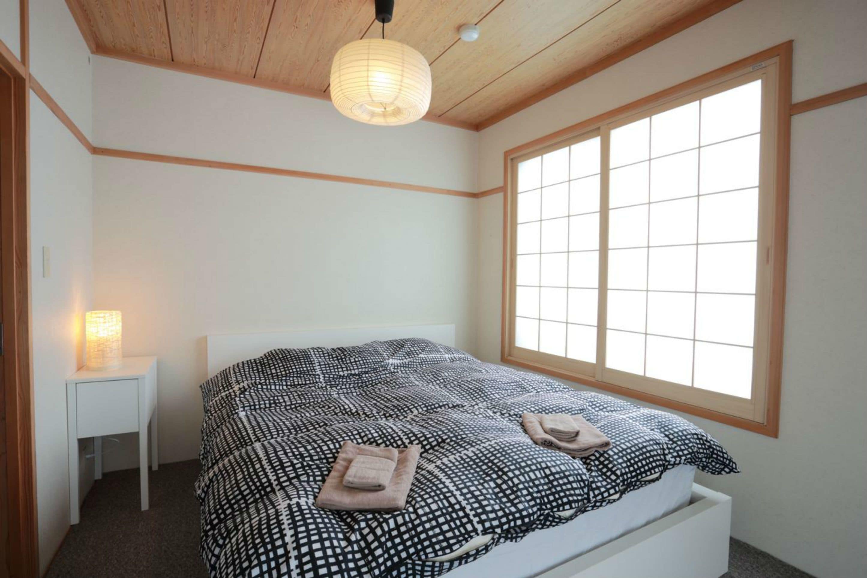 A bedroom with a bed, a bedside table with a lamp, and a large window.