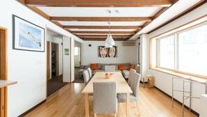 Un intérieur moderne avec un plancher en bois, une table à manger avec des chaises, un canapé et une grande fenêtre.