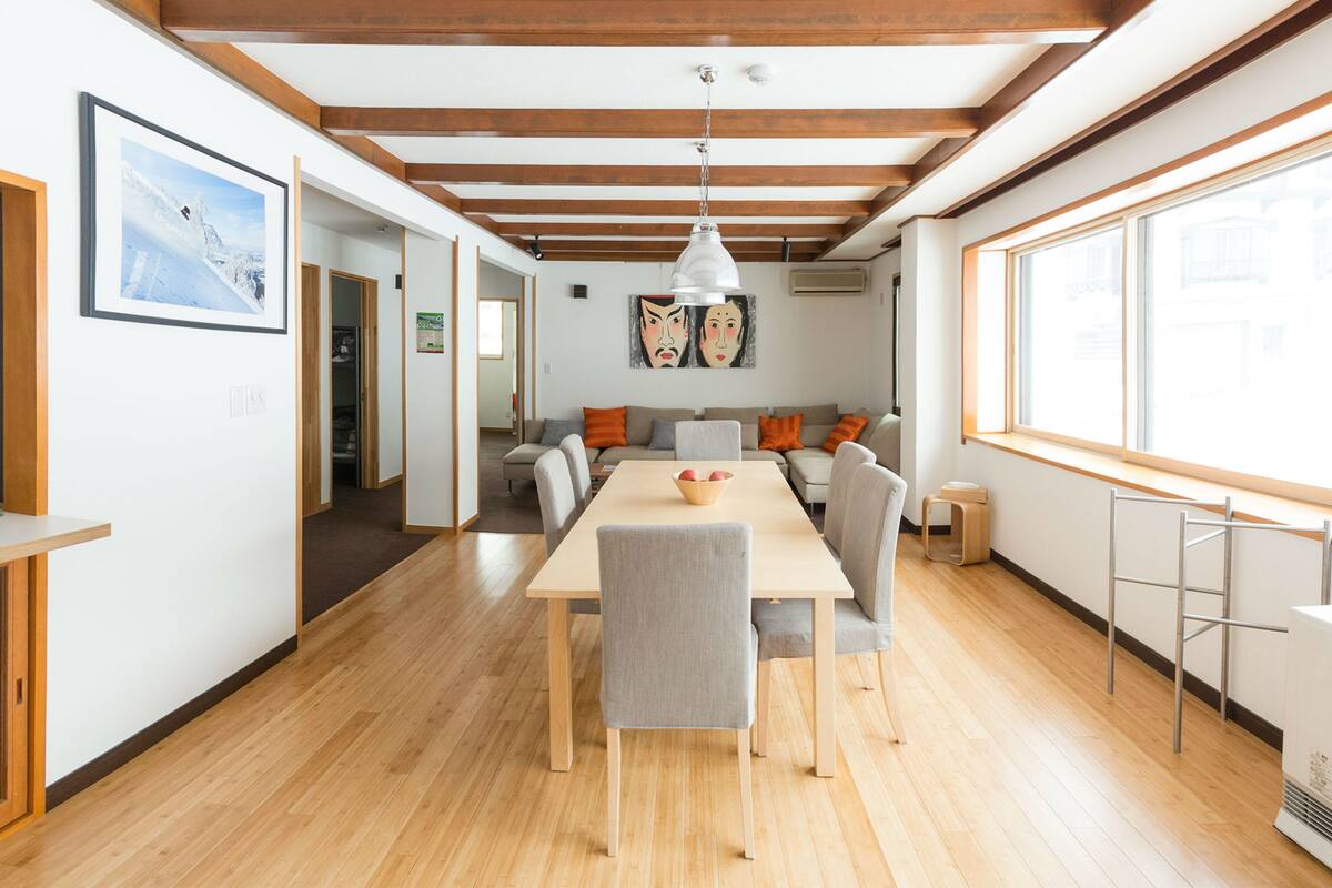Un intérieur moderne avec un plancher en bois, une table à manger avec des chaises, un canapé et une grande fenêtre.