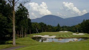 Un parcours de golf avec un étang, des arbres et des montagnes en arrière-plan.