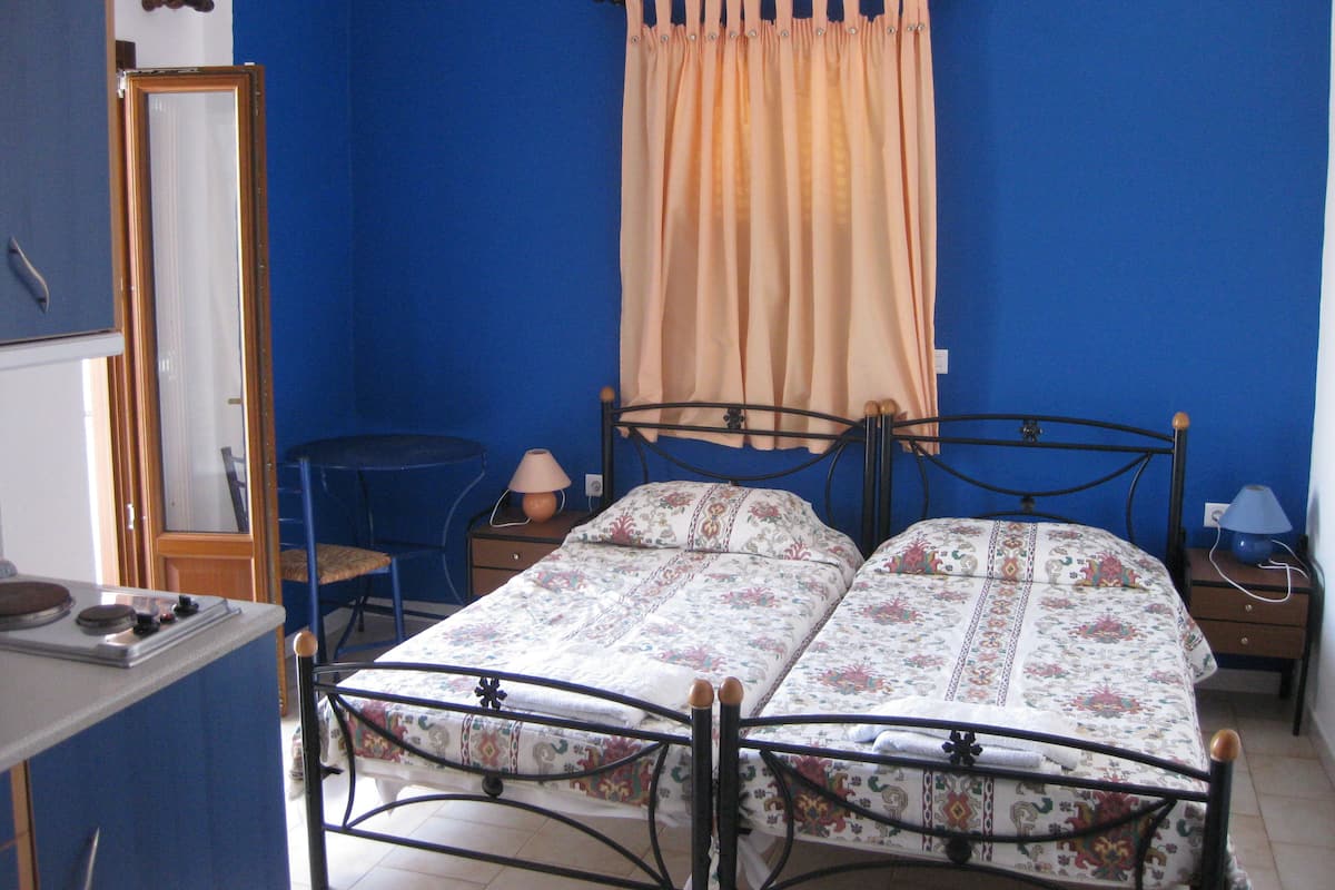 A bedroom with a double bed, a small table, a chair, a mirror, and a heater.
