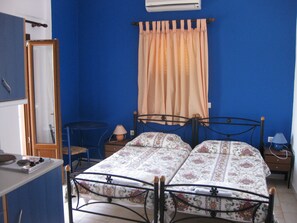 Un dormitorio con una cama doble, una mesita pequeña, una silla, un espejo y un calentador.