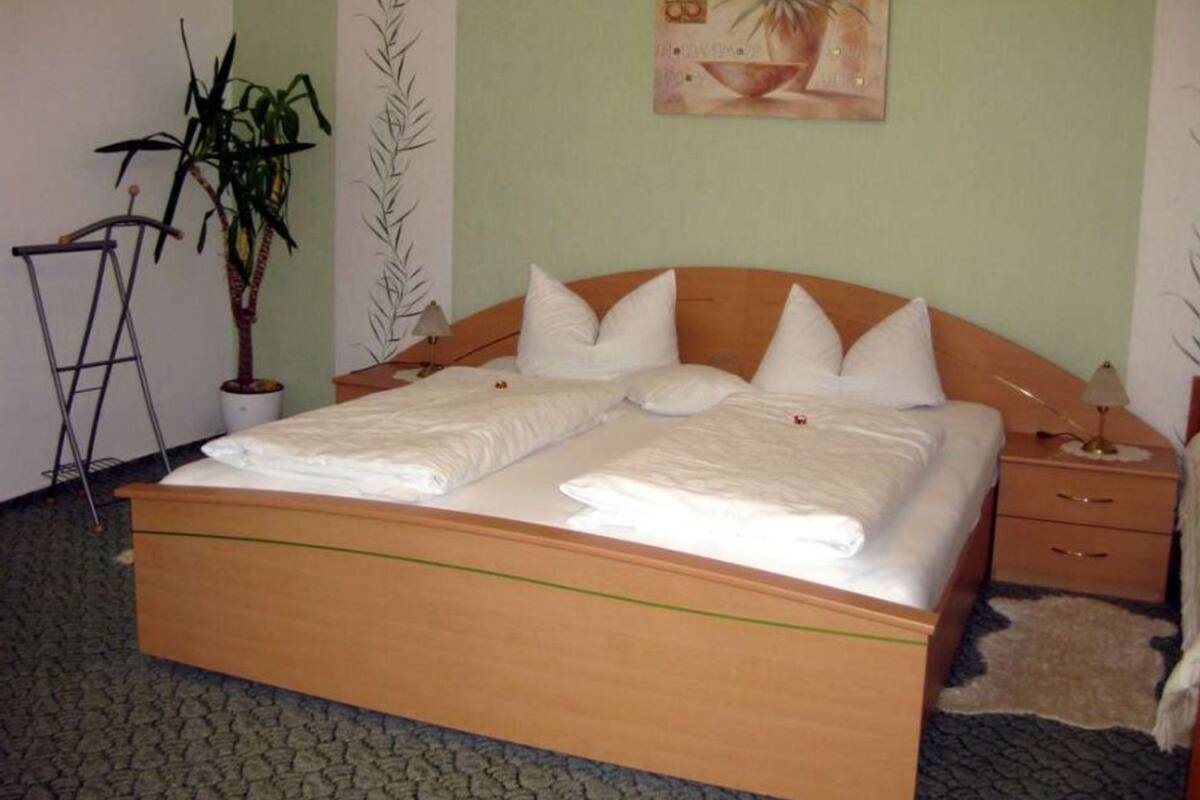 A neatly made bed with white linens, a wooden headboard, and a small bedside table with a lamp.