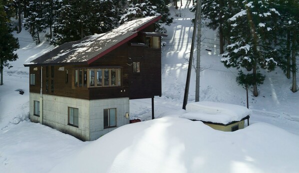 A two-story cabin with a red roof, surrounded by snow-covered trees and a snowy landscape. - Nozawa House (Nozawaonsen)