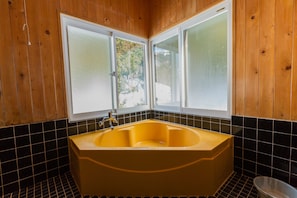 A bathroom with a bathtub, frosted glass windows, wooden walls, and black tiled flooring. - Nozawa House (Nozawaonsen)