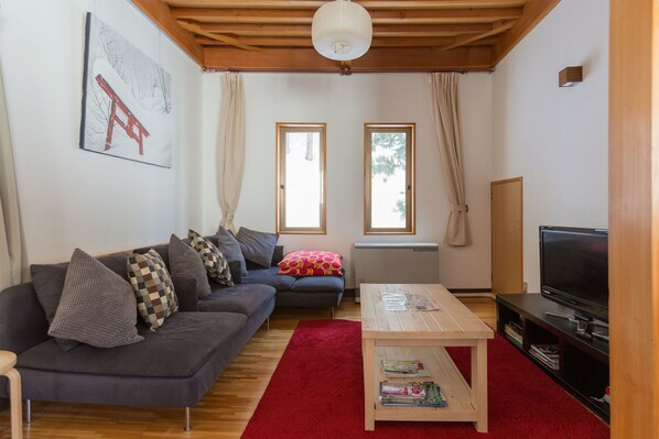 A living room with a sofa, a coffee table, a TV, and two windows.