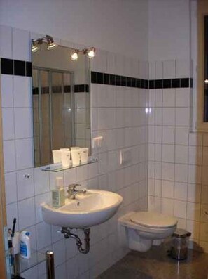 Un baño con azulejos blancos, un lavabo, un inodoro y un espejo.