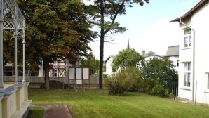 A residential area with a paved pathway leading to a white building, surrounded by trees and a fenced yard. - Villa Kaiserhof (Zinnowitz)
