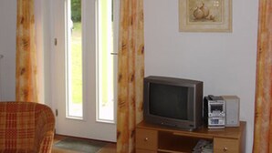A room with a television on a wooden stand, a framed picture on the wall, and a door with curtains. - Villa Kaiserhof (Zinnowitz)