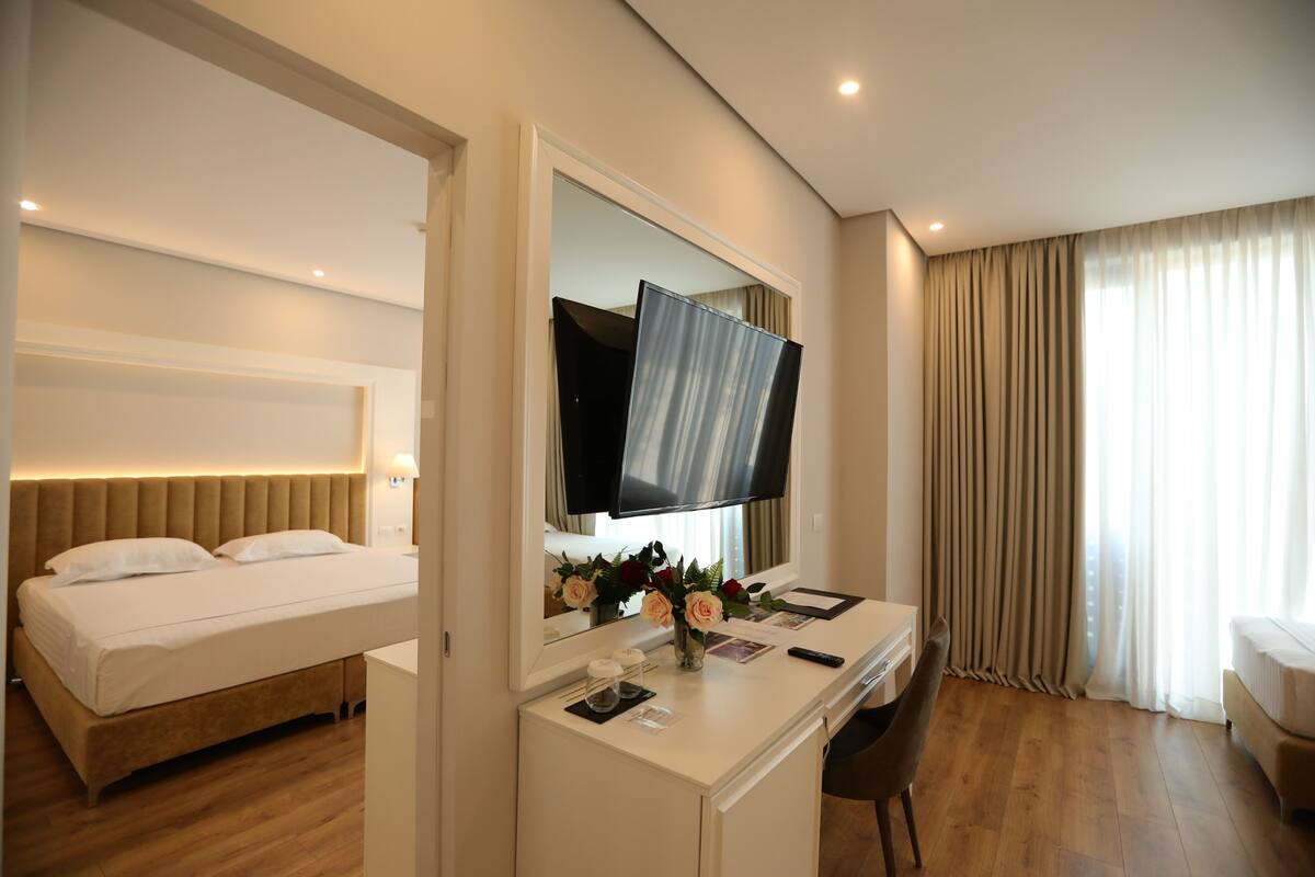 A hotel room with a bed, a desk with a chair, a television, and a large window with curtains.