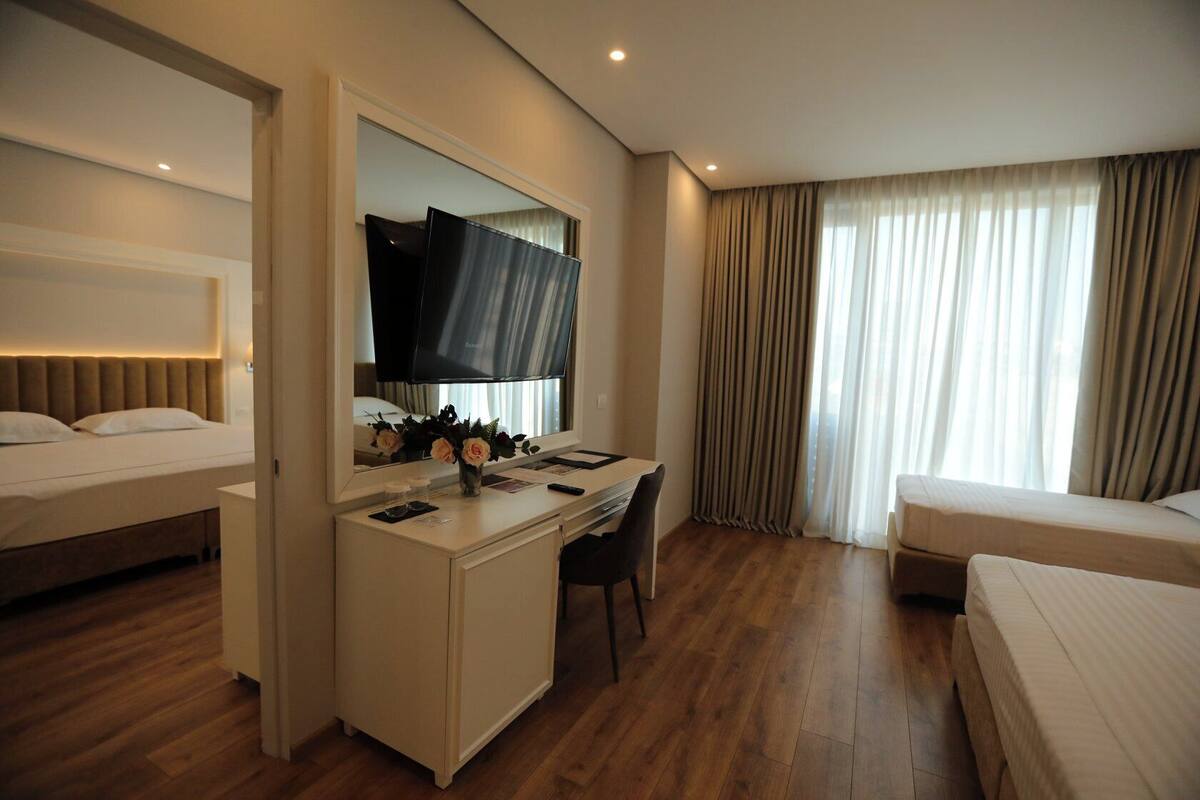 A hotel room with a bed, a desk with a chair, a television, and a window with curtains.