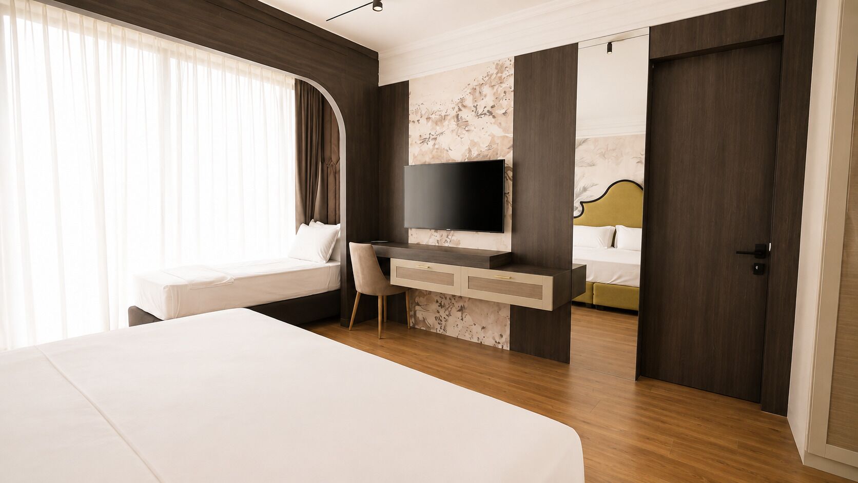 Ein modernes Hotelzimmer mit einem großen Bett, einem Schreibtisch mit Fernseher und einer Tür zu einem weiteren Raum.