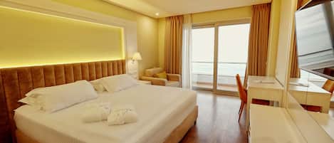 A hotel room with a large bed, a desk, a chair, and a view of the sea through the window.