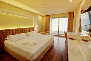 A hotel room with a large bed, a desk, a chair, and a view of the sea through the window. - Premium Beach Hotel (Golem)