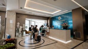A hotel reception area with marble flooring, a reception desk, and a wall-mounted sign. - Premium Beach Hotel (Golem)