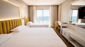 A hotel room with two beds, a desk, a chair, a television, and a view of the sea. - Premium Beach Hotel (Golem)