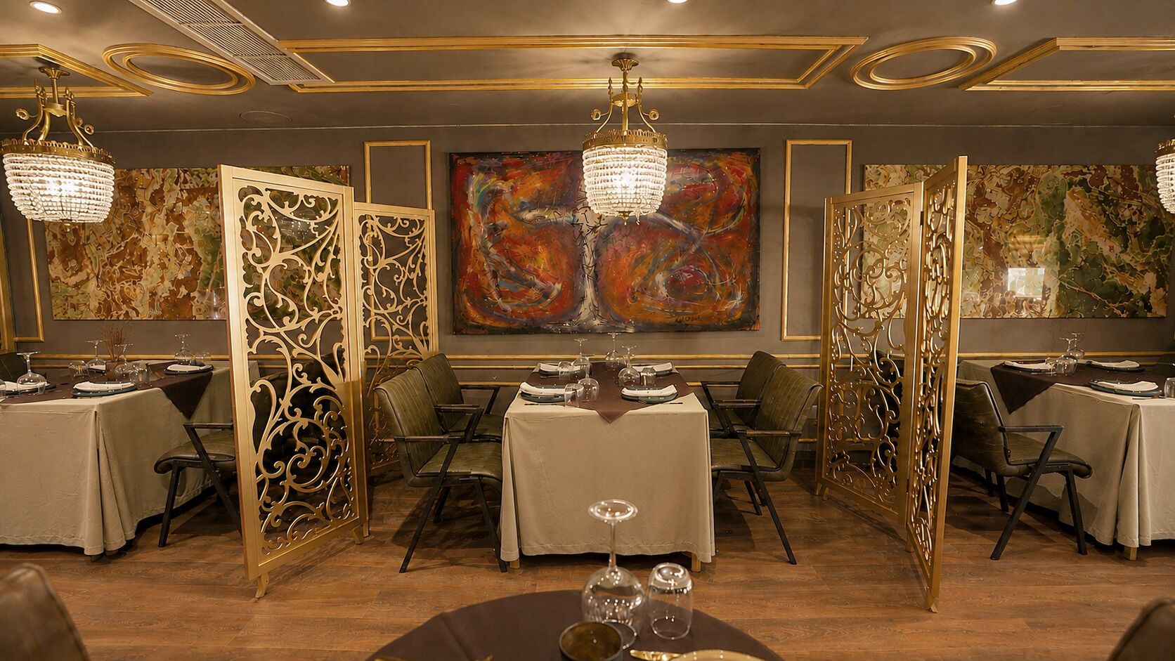 Un comedor con mesas dispuestas para el servicio, paneles decorativos y un cuadro abstracto grande en la pared.