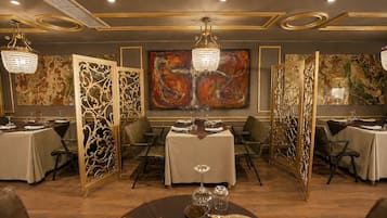 Un comedor con mesas dispuestas para el servicio, paneles decorativos y un cuadro abstracto grande en la pared.