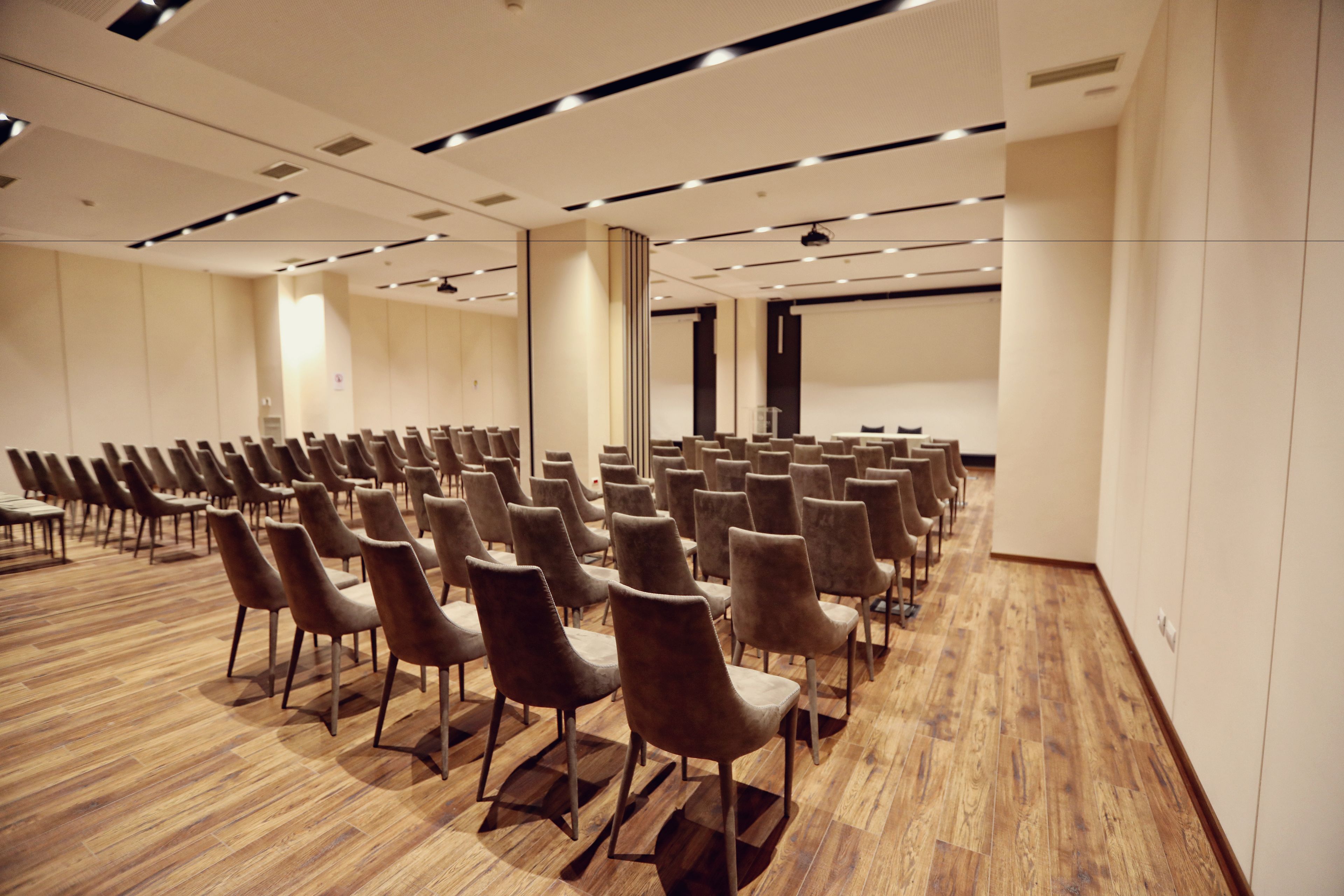 A conference room with rows of chairs, a wooden floor, and a projector screen.