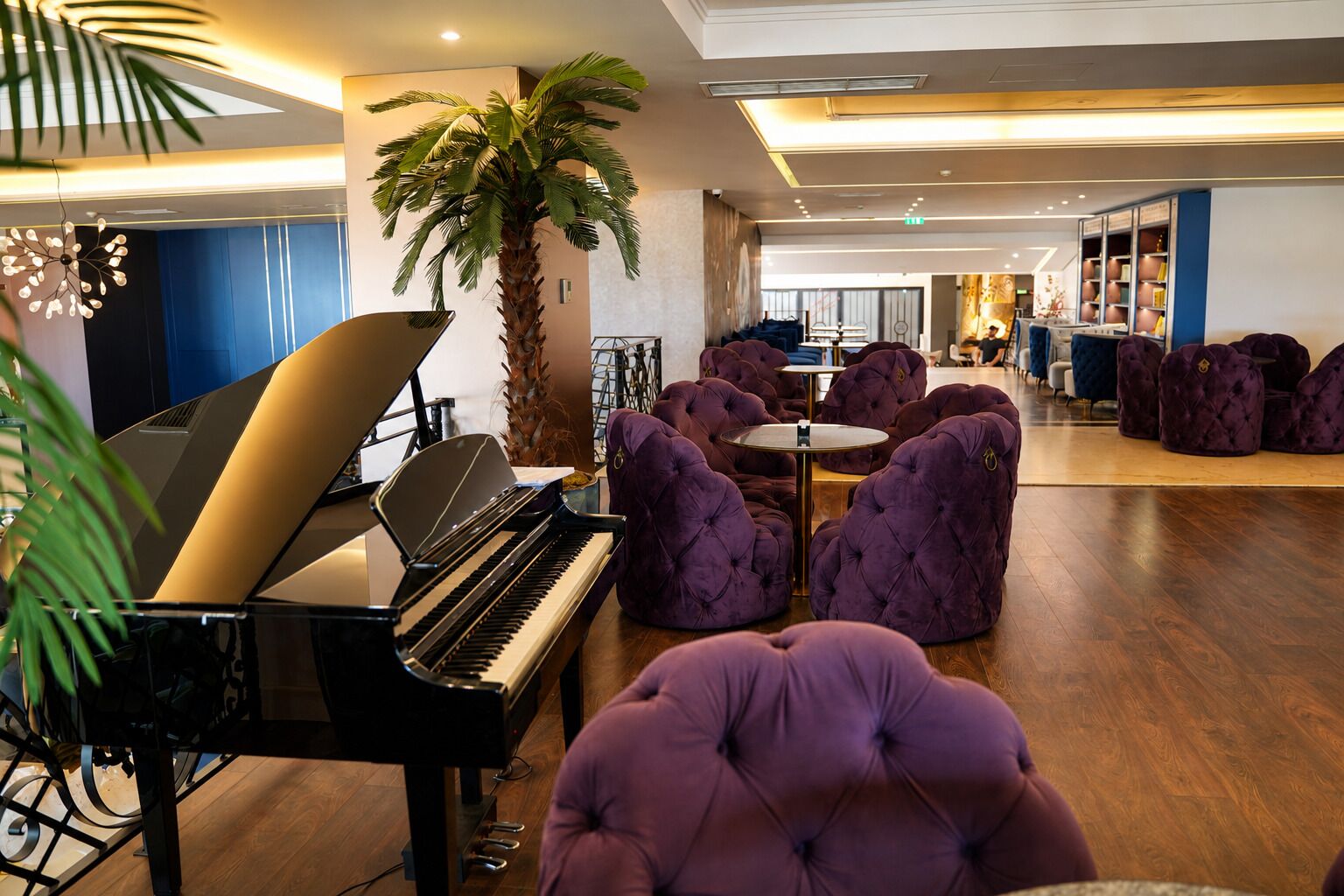 A lobby with a grand piano, plush purple seating, a palm tree, and a modern interior design.