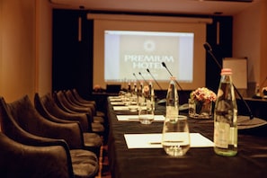 A conference room with a long table, chairs, microphones, water bottles, and a screen displaying "PREMIUM HOTEL". - Premium Beach Hotel (Golem)