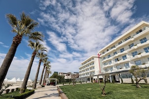 Un hotel moderno con techo plano, varios balcones y un césped bien cuidado con palmeras.
