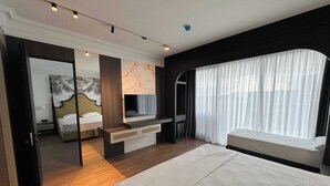 Una habitación de hotel moderna con cama, televisor, escritorio y un gran ventanal con cortinas.
