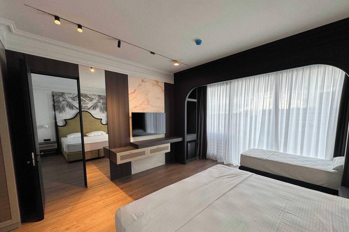 A modern hotel room with a bed, a TV, a desk, and a large window with curtains.