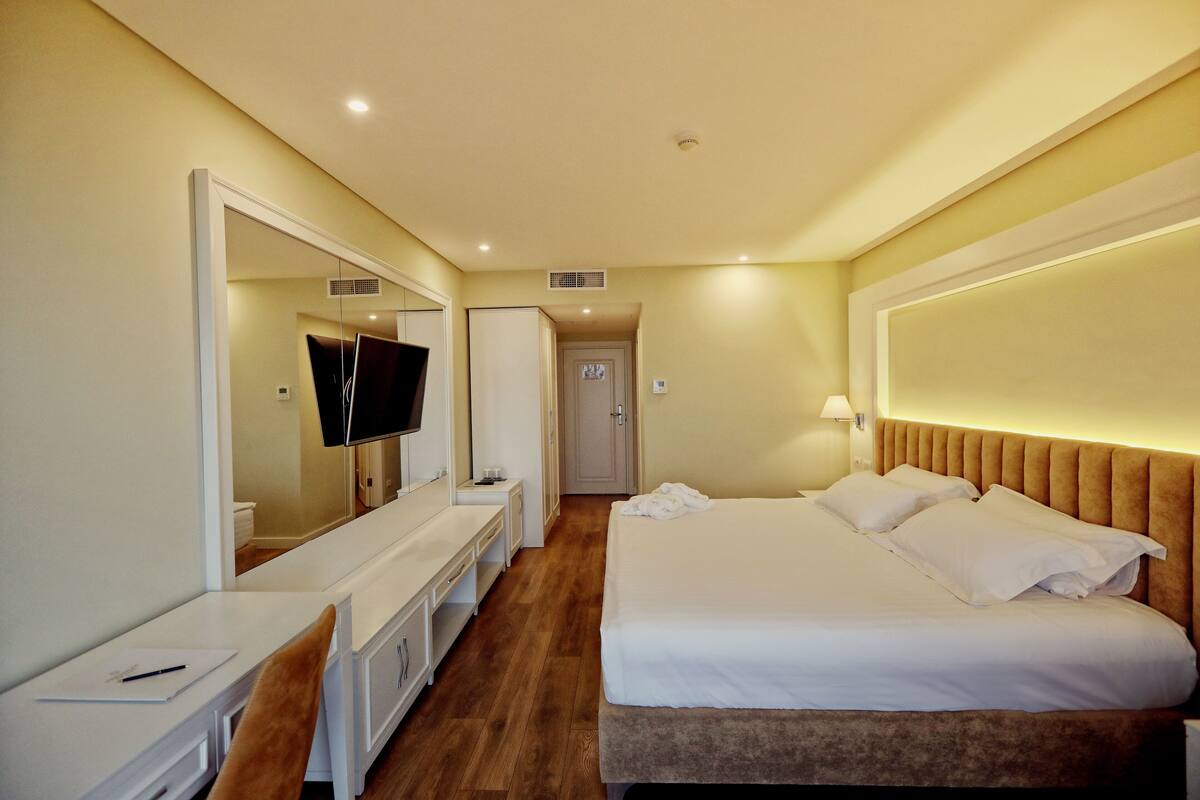 A hotel room with a bed, a desk, a TV, and a mirror.