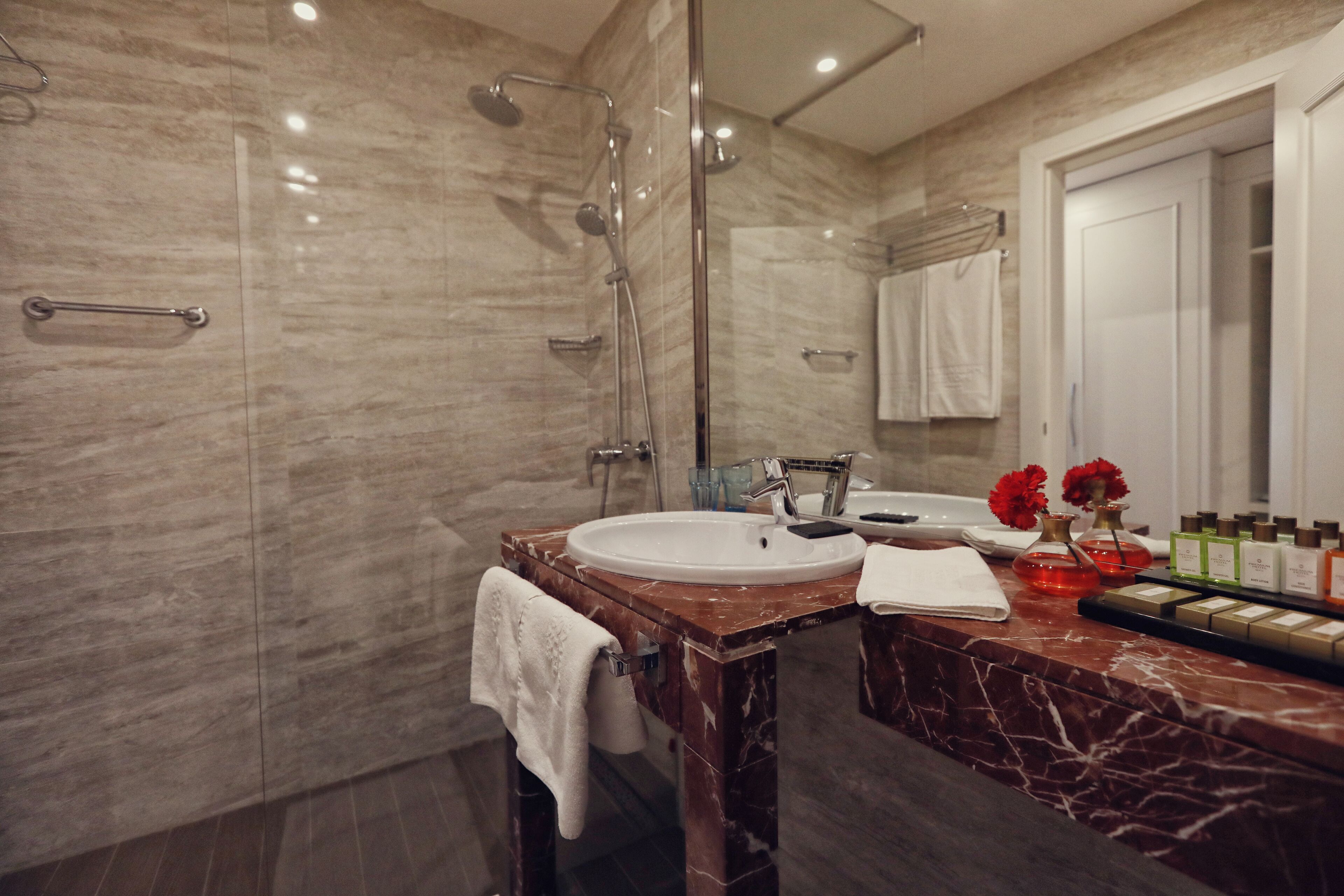 Un bagno moderno con lavabo in marmo, box doccia in vetro e mobile contenitore con articoli da toilette.