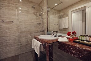 A modern bathroom with a marble sink, a glass shower enclosure, and a vanity with toiletries. - Premium Beach Hotel (Golem)
