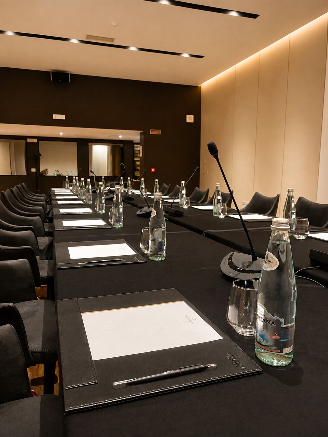 A conference room with a long table, chairs, microphones, water bottles, and nameplates.