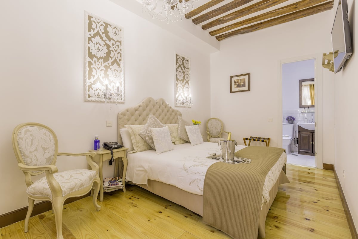 A bedroom with a large bed, a chair, a bedside table, and a small bathroom visible through an open door.